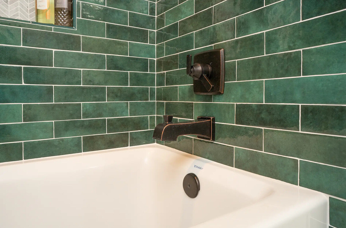 Tub with green subway tile and built-in shower shelf in bathroom by Imagine Remodeling